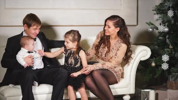 Parents and their little children are sitting on the sofa near the decorated Christmas tree — Stock Video