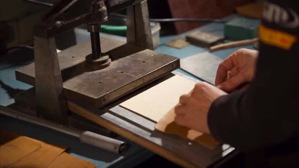 Ремесленник кладет металлическую пластину для штамповки кожаной детали в мастерскую — стоковое видео