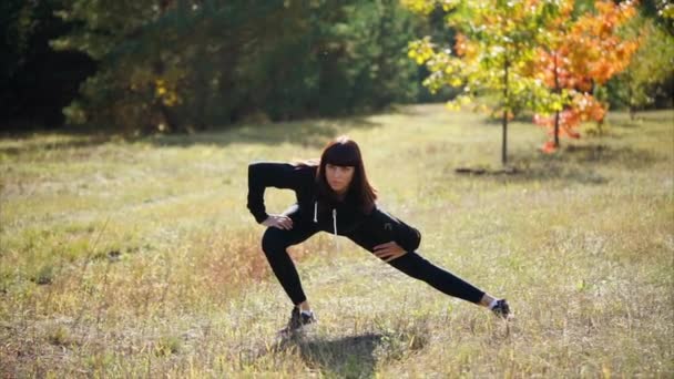 En kvinna i en sport kostym sträcker sina muskler innan träningen i en sommar park — Stockvideo