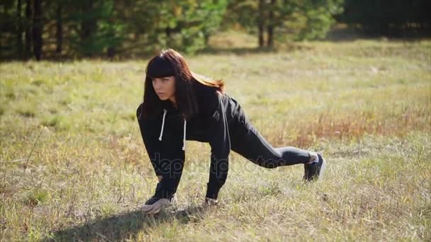 Молодая женщина в костюме согревает мышцы ног перед тренировкой на природе — стоковое видео