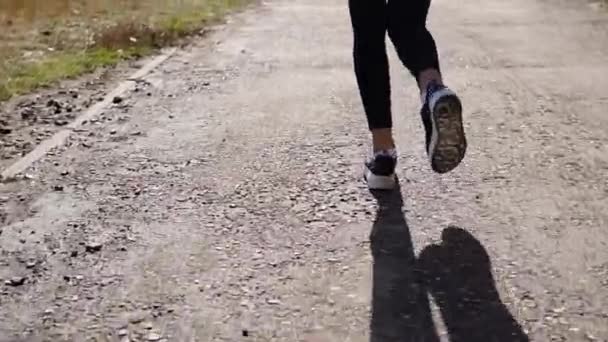 Πόδια του λεπτή γυναίκα κάνει τζόκινγκ σε ένα κομμάτι σε ηλιόλουστη μέρα, ΠΙΣΩ ΟΨΗ — Αρχείο Βίντεο