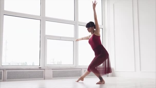 Танцовщица репетирует танец в зале с большими окнами днем — стоковое видео