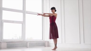 Modern dansçı klasik bale konumlarını, beyaz bir salonda ayakta gerçekleştiriyor