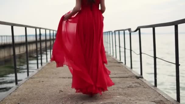 Szczęśliwy uroda w sukni szkarłat idzie na obcasie czerwone wzdłuż morza molo — Wideo stockowe
