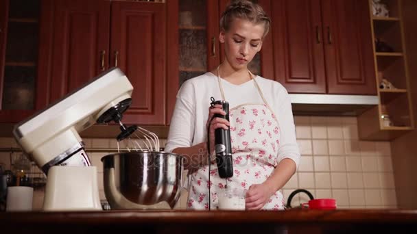 Jonge vrouw die thuis zweepslagen creamer in de keuken met een mixer bereidt — Stockvideo