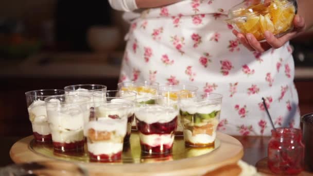 O cozinheiro coloca pedaços de fruta dentro dos copos com creme de decoração com laranjas — Vídeo de Stock