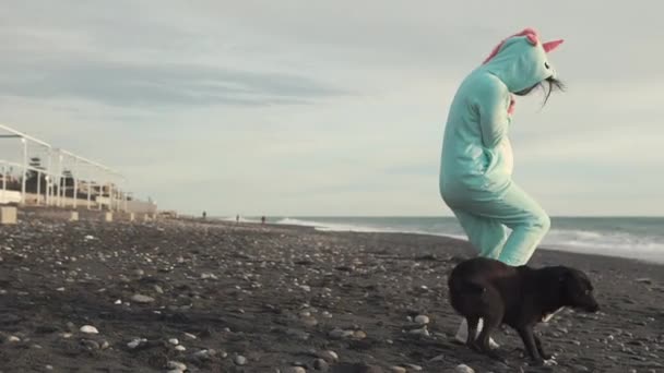 Eine fröhliche Dame im kigurumi-Kostüm amüsiert sich mit einem Hund am Meer — Stockvideo