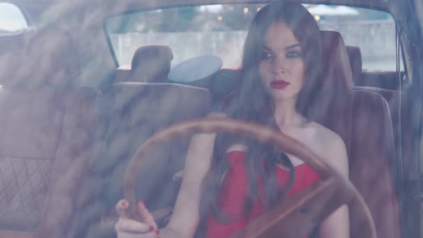 Glamourous brunette με τα κόκκινα χείλη κάθεται σε ένα κάθισμα οδήγησης σε ένα αυτοκίνητο — Αρχείο Βίντεο