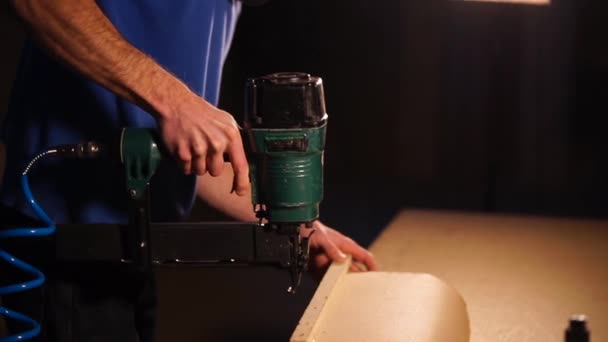 Ξυλουργός ενισχύει μια ξύλινη σανίδα στη βάση των επίπλων με συρραπτικό — Αρχείο Βίντεο