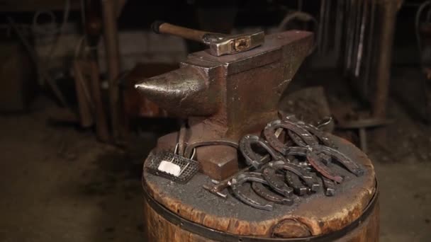 Finished horseshoes are lying in a heap near an anvil on old wooden stand — Stock Video