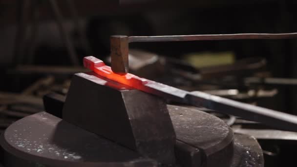 Працівник штампує вирізи на нагрітій металевій деталі в кузнях, з молотком — стокове відео