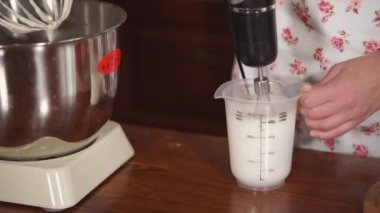 Kadın krem mutfak masasında Kupası'nda karıştırma için elektrikli bir çırpma teli kullanıyor