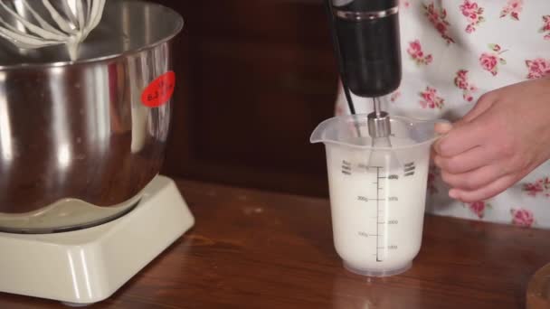 Жінка використовує електричне вуса для змішування вершків у чашці, на кухонному столі — стокове відео