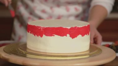Dekoratör şekerleme, kek yanağında üzerinde kırmızı tereyağı krema uyguluyor