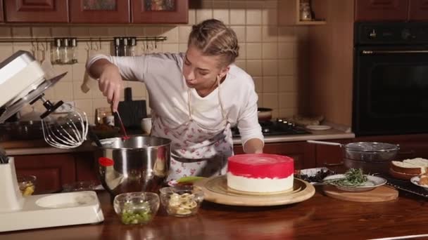 Junge Frau ist Hobby-Konditorin dekoriert Kuchen mit roter Buttercreme — Stockvideo