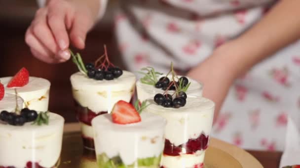 Cook is decorating desserts in glasses, by strawberry, whipped cream, chokeberry — Stock Video