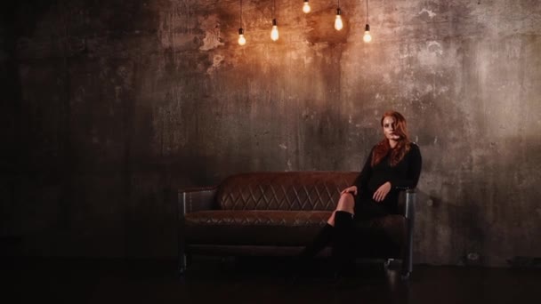Charmiga unga kvinnan är att placera i en soffa i mörkt tomma rum — Stockvideo