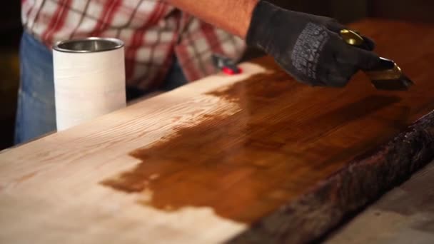 Человек наносит коричневый лак на поверхность деревянной доски, покрасочный цех — стоковое видео