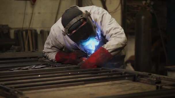 Soldador de gas está en una tienda de la planta, inclinándose sobre vigas de metal y soldadura — Vídeos de Stock