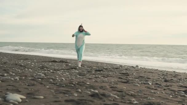 Gekke vrouw draagt kigurumi kostuum van de eenhoorn wordt uitgevoerd over strand — Stockvideo