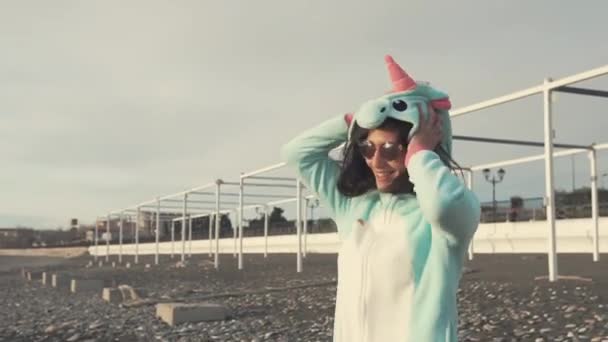 Cheerful girl is wearing blue kigurumi of unicorn and jumping on beach — Stock Video