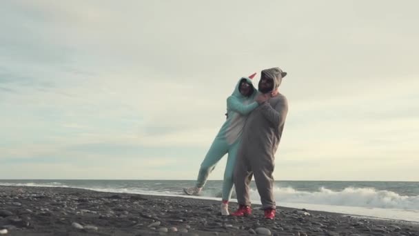 Мужчина поднимает свою девушку, как в кигуруми, так и на пляже у моря — стоковое видео