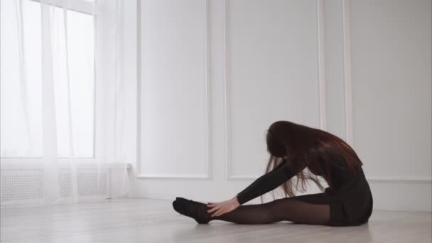 Young and pretty woman stretching leg muscles on the floor in the studio — Stock Video