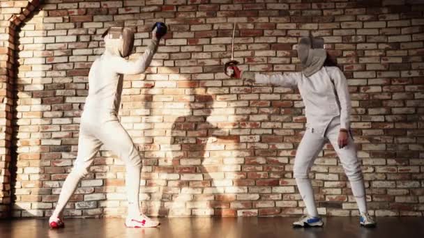 Два фехтовальщика тренируются против кирпичной стены в помещении — стоковое видео