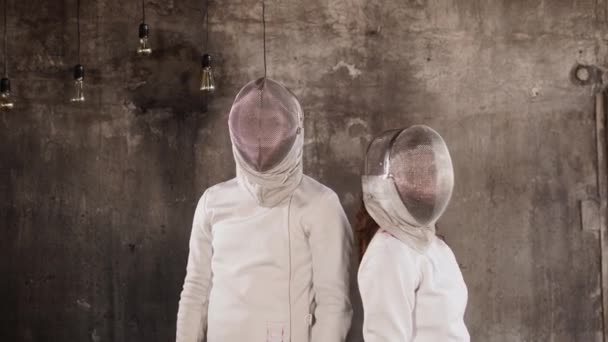 Portrait de deux jeunes escrimeurs en costumes et masques, debout près d'un mur gris — Video