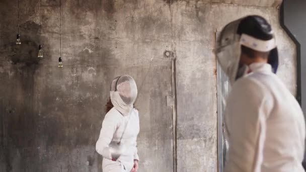 Dos jóvenes esgrimistas practican embestidas y ataques con sables en un salón oscuro — Vídeo de stock