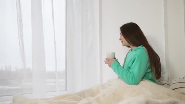 Mujer joven y bonita está tomando café en su cama por la mañana — Vídeo de stock