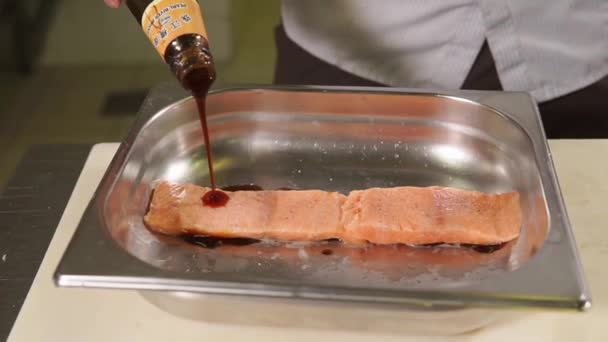 Cook está derramando molho chinês de garrafa para filé de salmão em uma placa de metal — Vídeo de Stock