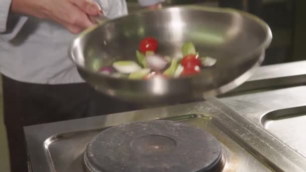Кук жарит овощи на большой сковородке, бросает их — стоковое видео
