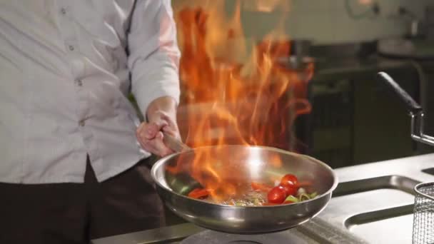 Cook is flambeing vegetables in a saute pan, tossing it up , close-up — Stock Video