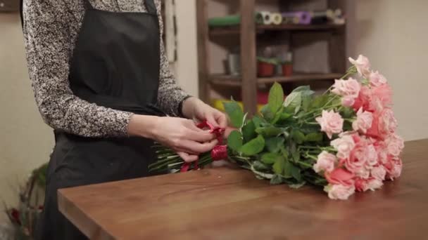 Bliska strzał rąk womans, który więzi różową wstążką do bukiet róż — Wideo stockowe