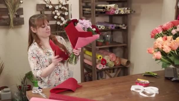 Floristería recoge arreglos florales, una mujer pone un papel brillante — Vídeos de Stock