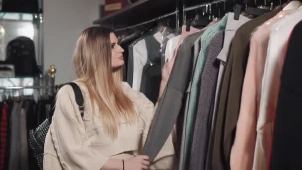 En vacker kvinna ser ut i en varm cardigan som finns i en modern boutique — Stockvideo