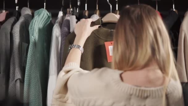 A young woman is considering a warm sweater, on which a tag with a price weighs — Stock Video