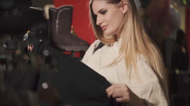Ensam kvinna är i en designbutik med kläder, att pröva plagget på galge — Stockvideo
