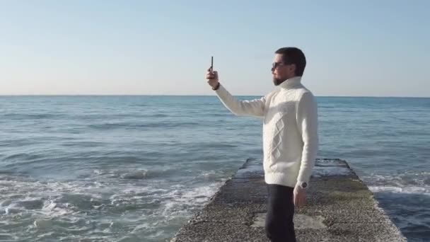 L'uomo è in piedi su un frangiflutti di pietra e riprese video da smartphone — Video Stock