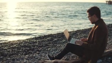 Ciddi adam dizüstü bilgisayar ile bir kumsalda oturuyor