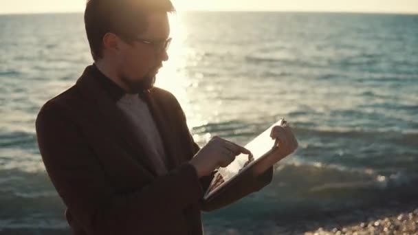 Hombre adulto trabajando en una tableta portátil, hombre de negocios de pie junto al mar — Vídeo de stock