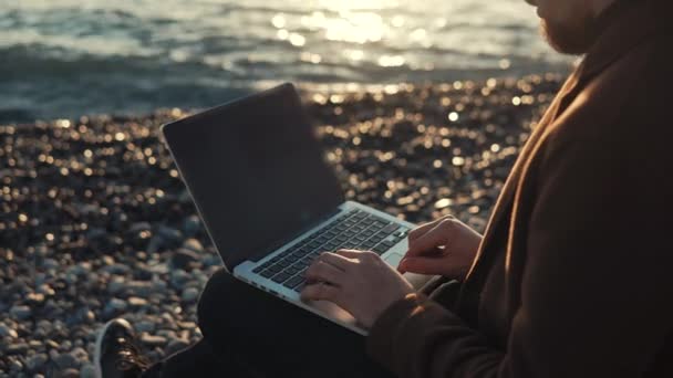 Scrittore moderno sta digitando sulla tastiera del notebook sullo sfondo della marea marina — Video Stock