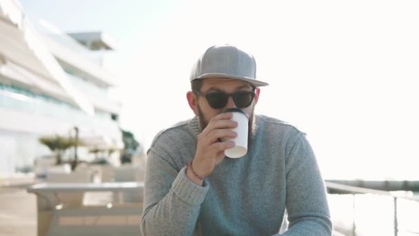 Bebaarde hipster drinkt koffie buiten — Stockvideo