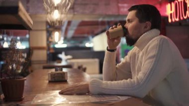 sıcak kazaklı genç bir adam bir barda karton bir fincan sıcak kahve içer