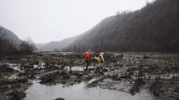 Hombre y él amigos en chaquetas de otoño tratando de cruzar el pantano en la lluvia — Vídeo de stock