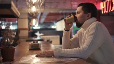 sıcak kazaklı genç bir adam bir barda karton bir fincan sıcak kahve içer