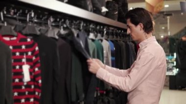 Koyu saçlı adam Giyim Askıları trendy dükkanda üzerinde arıyor
