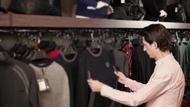 Un jeune homme regarde le matériel d'un pull dans une boutique chère — Video