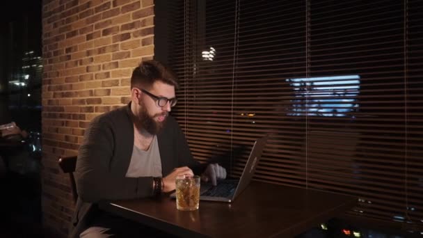 Дорослий чоловік працює в барі за ноутбуком і п'є алкогольний напій — стокове відео